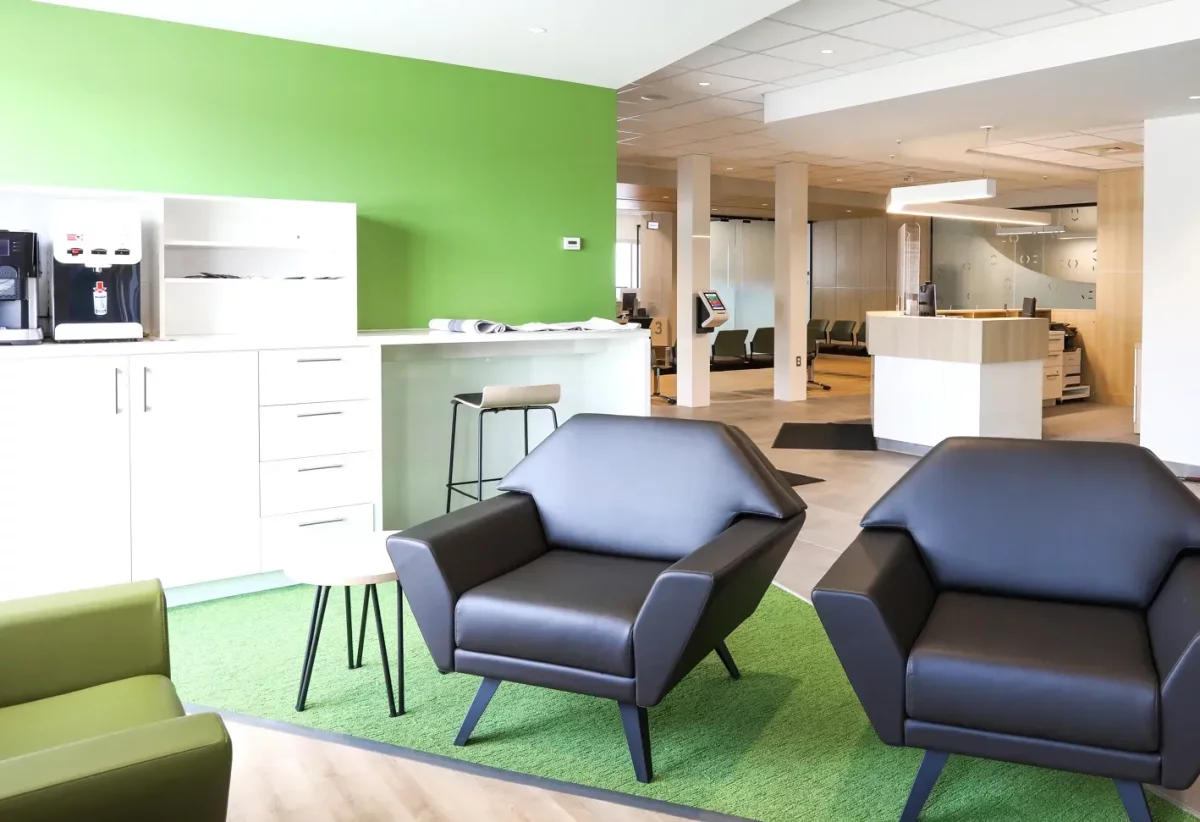 Salon avec sofas noirs, mur vert Desjardins et comptoir d'accueil en bois – rénovation intérieure Lanaudière par BGC