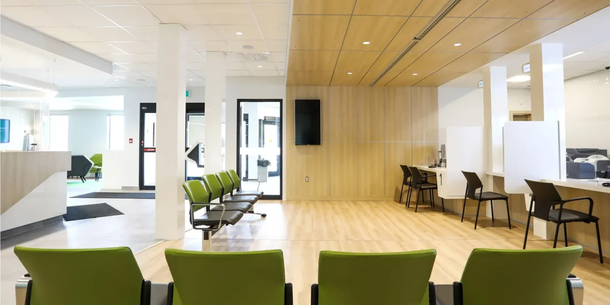 Salle d'attente avec chaises vertes, mur de bois et écran – aménagement intérieur Desjardins Saint-Félix-de-Valois