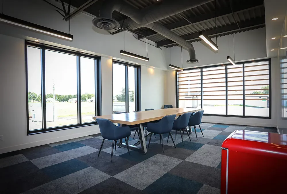 Salle de conférence moderne avec table en bois, fenestration abondante et plafond industriel en structure d'acier