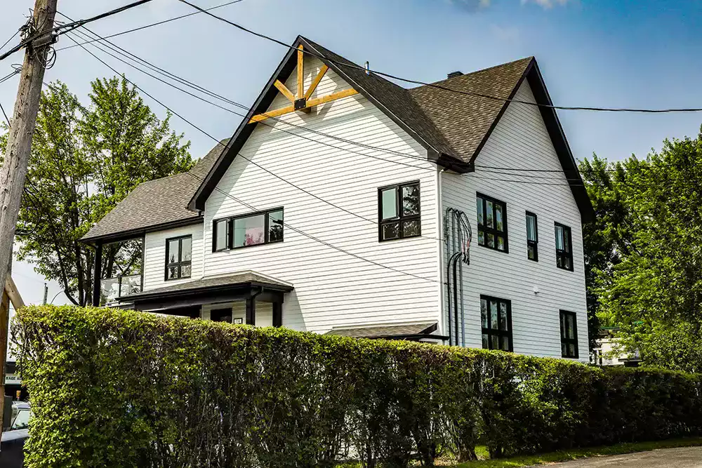 Façade avant du triplex blanc avec fenêtres noires et haie de cèdres – construction multi-résidentielle Ste-Elizabeth