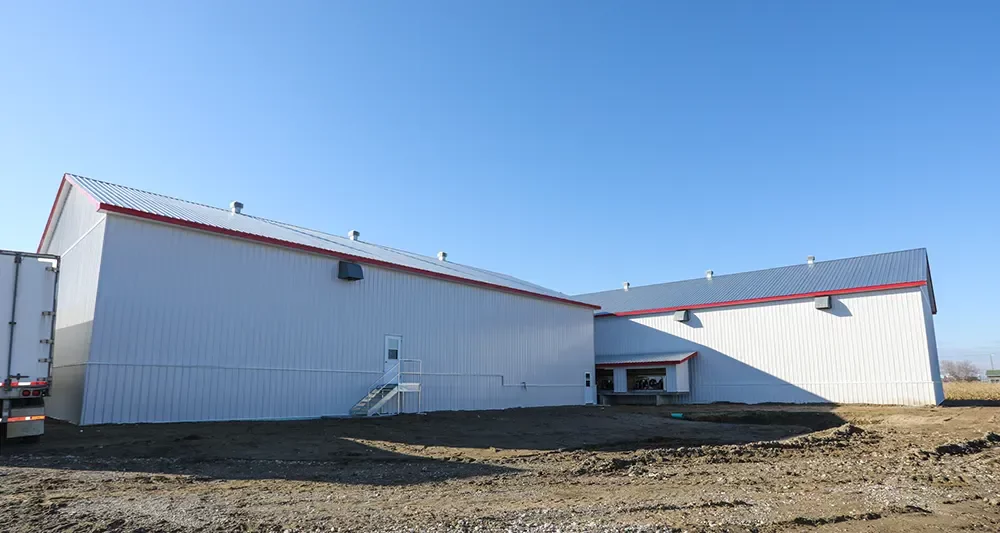 Vue latérale de l'entrepôt agricole blanc avec accents rouges – projet Ferme Jobin & Roberge Saint-Alexis par BGC