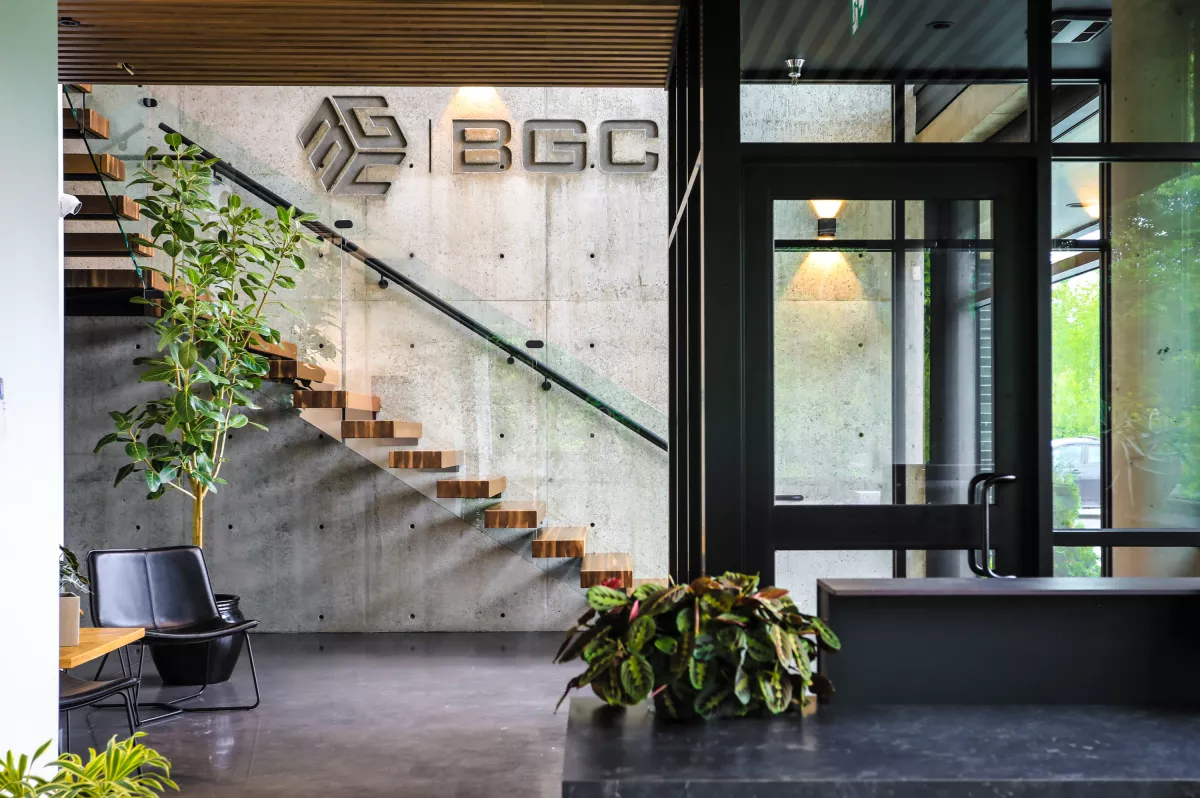 Entrée du siège social BGC avec logo sur mur de béton, escalier flottant en bois et garde-corps en verre