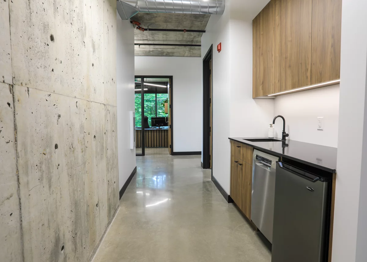 Corridor avec mur de béton brut, cuisinette en bois et plancher époxy