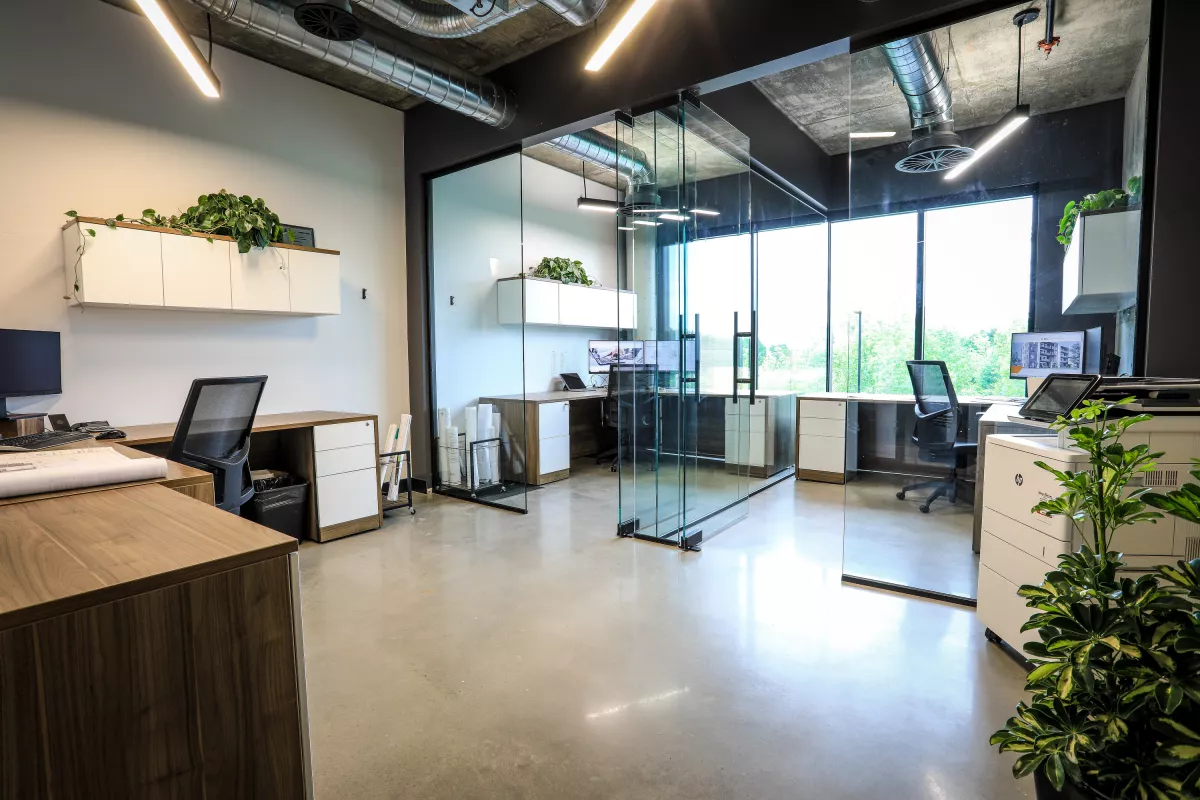 Aire ouverte avec bureaux, cloisons vitrées, plantes et conduits apparents