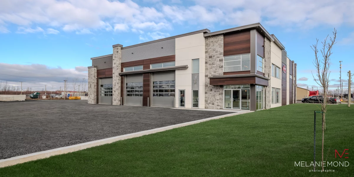 Vue de la façade complète avec pierre grise, bois et stationnement – bâtiment commercial Épandage YFL par BGC