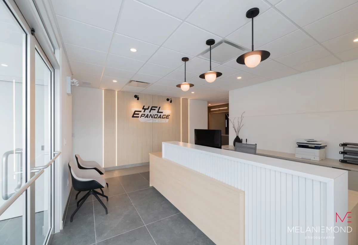 Aire de réception moderne avec comptoir blanc, logo YFL et luminaires suspendus – bureaux Épandage YFL Joliette
