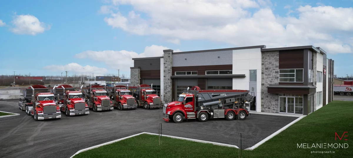 Flotte de camions rouges Épandage YFL stationnés devant le bâtiment – construction commerciale Joliette par Gestion BGC