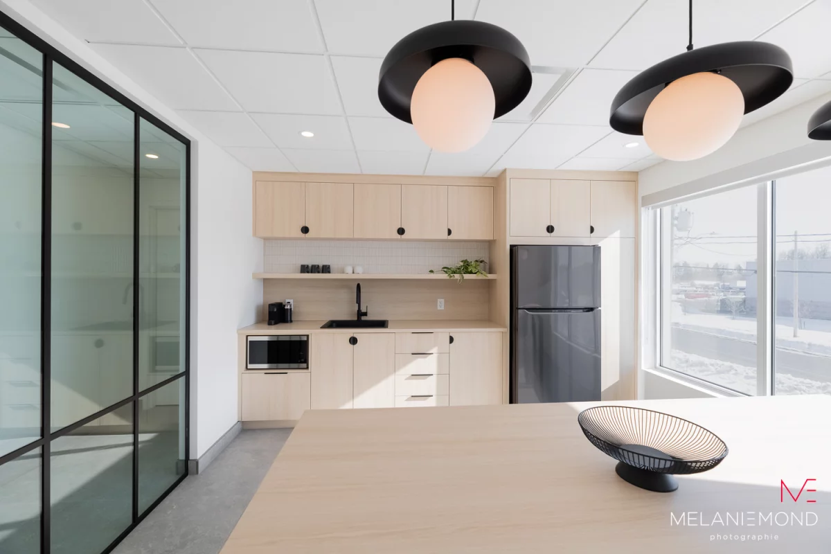 Cuisine des employés avec armoires de bois clair, luminaires noirs et grande table – bureaux Épandage YFL par BGC