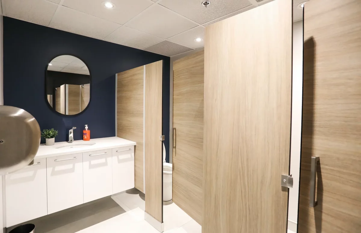 Salle de bain moderne avec mur bleu marine, miroir rond et finitions en bois – rénovation commerciale BGC