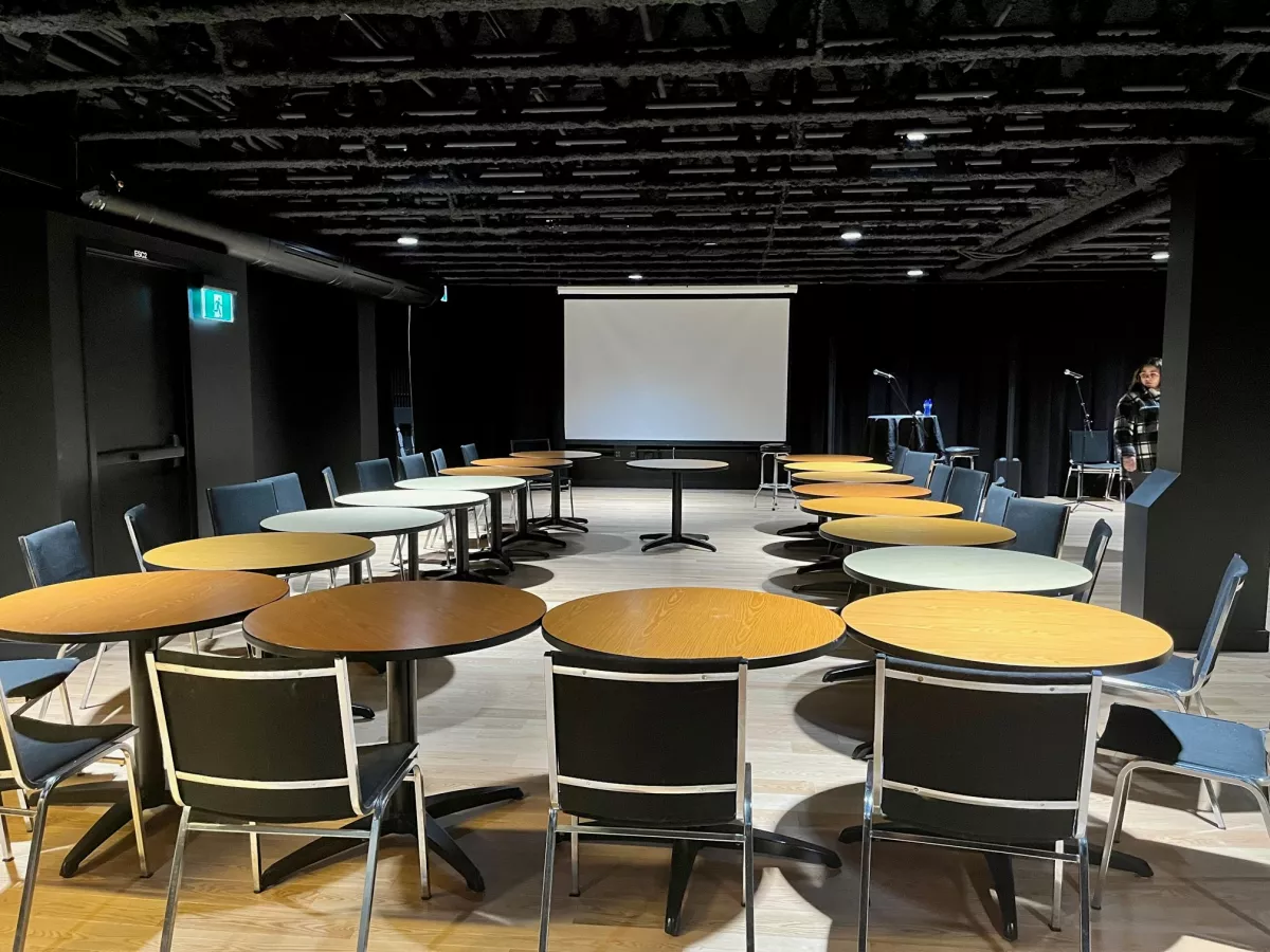 Salle de conférence avec écran de projection, tables rondes et plafond noir
