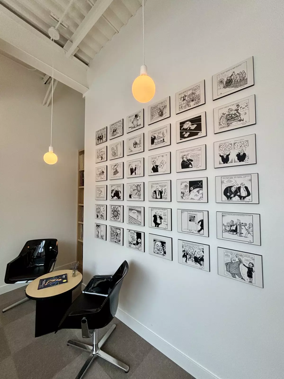 Coin lecture avec mur de caricatures encadrées et fauteuils design noirs