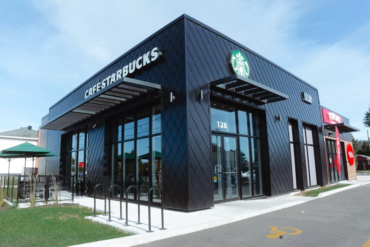 Façade du Starbucks Saint-Charles-Borromée avec revêtement noir, parasols verts et mur en bois