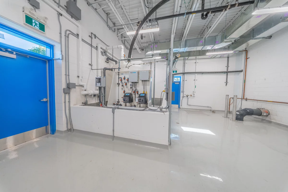Salle mécanique avec tuyauterie, équipements de traitement et porte étanche bleue