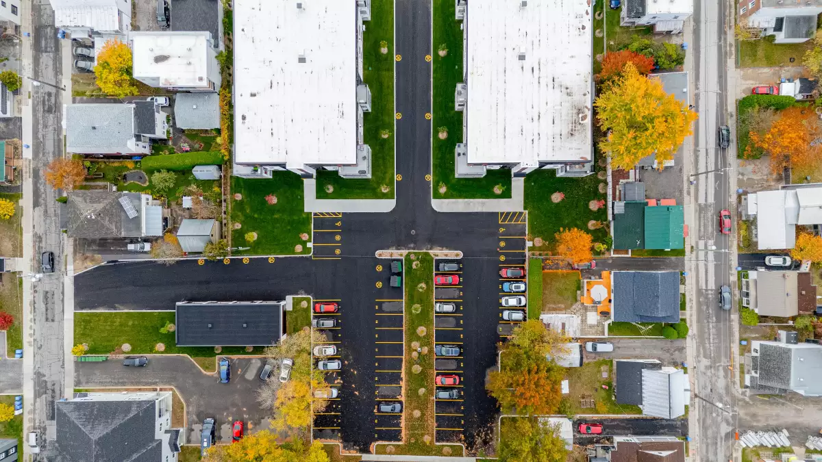 Vue aérienne plongeante du complexe multi-logements avec stationnements et toits plats
