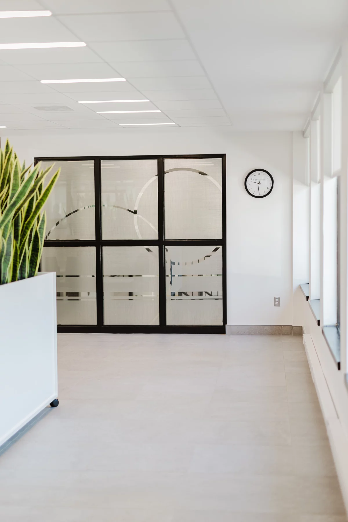 Hall d'accueil avec portes vitrées givrées, jardinière de sansevieria et horloge murale – aménagement BGC Lanaudière