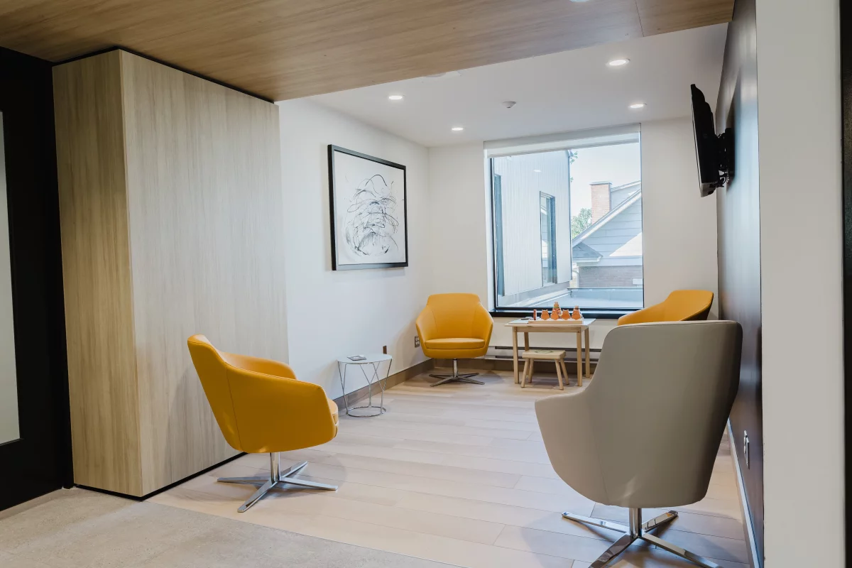Salon d'attente avec fauteuils jaunes, coin enfants et plafond en bois – Desjardins Saint-Félix-de-Valois par BGC