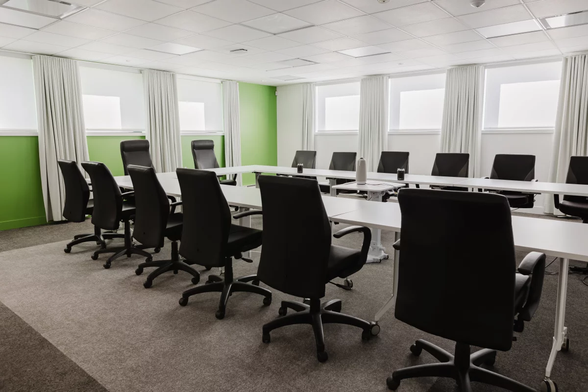 Salle de conférence avec murs verts, rideaux blancs et chaises ergonomiques – aménagement commercial BGC