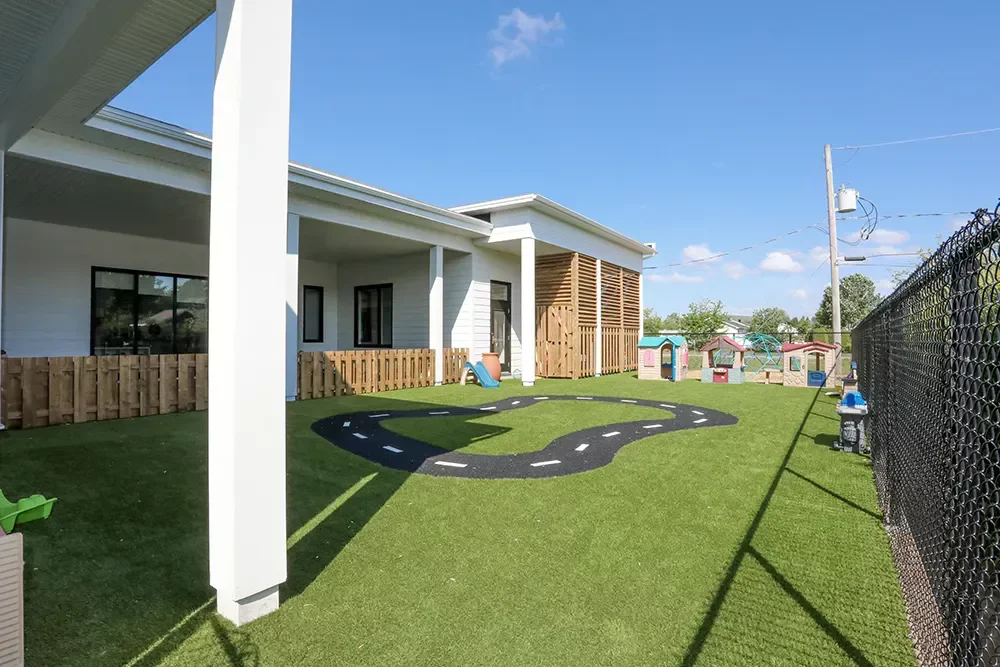 Aire de jeux extérieure avec piste de circulation sur gazon synthétique et clôture de bois – construction BGC