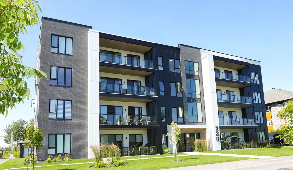 Immeuble locatif luxueux avec balcons, briques grises et aménagement paysager soigné – construction BGC Lanaudière